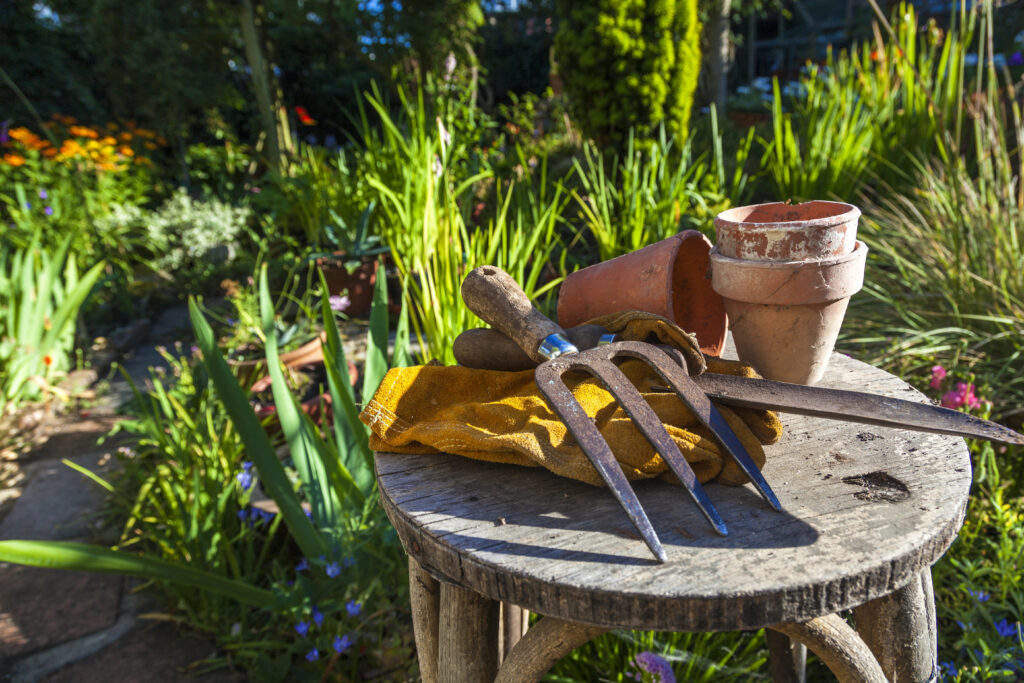 Image of garden tools, clay pots, and gardening gloves on a table in a garden.